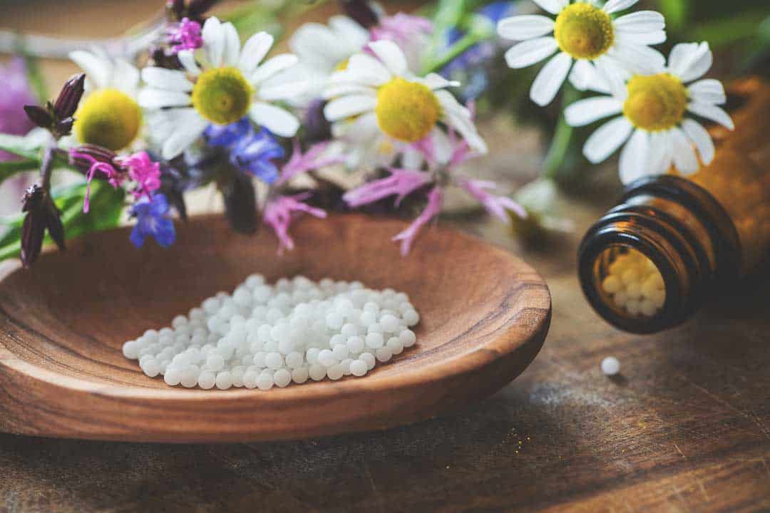 Homeopathic remedies with flowers Homeopathic remedies with flowers and herbal pills on a wooden surface.